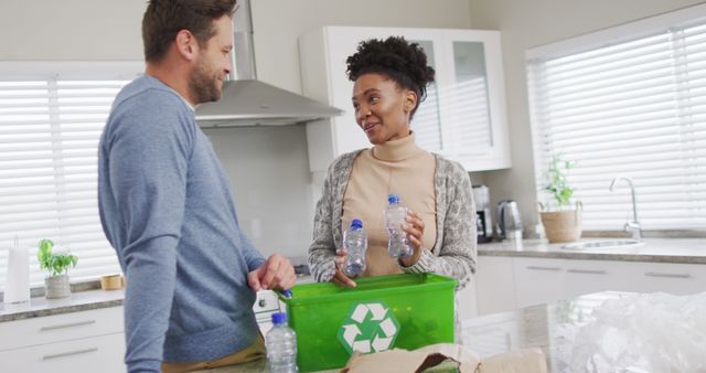 Couple standing in the kitchen recycling plastic bottles, encouraging sustainability practices at home. Useful for projects related to eco-friendly habits, environmental awareness, and promoting green living initiatives.