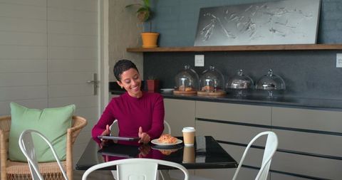 Mid adult woman smiling and working on tablet in modern cafe with pastry and takeaway coffee
