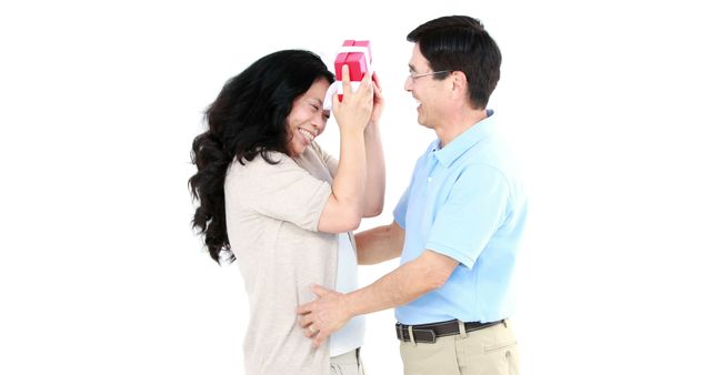 A middle-aged Caucasian man surprises a woman with a gift, both sharing a joyful moment, with copy space. Their smiles and playful interaction suggest a celebration or a special personal event.