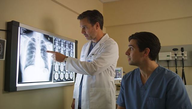 Physician pointing at chest x-ray while trainee reviewing ct scans in hospital