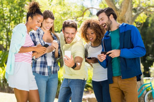 Group of friends taking a selfie with a mobile phone in a park. They are smiling and appear to be enjoying their time together. This image can be used for promoting social activities, friendship, outdoor events, and lifestyle content.