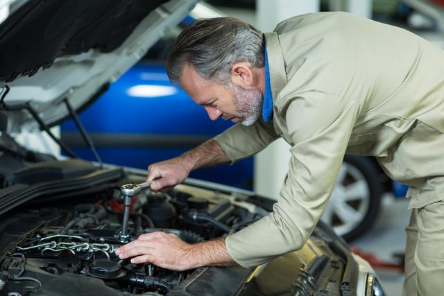 A professional mechanic working on a car engine inside a repair garage. Suitable for use in articles about car maintenance, mechanics, automotive repair services, and DIY car repair tips.