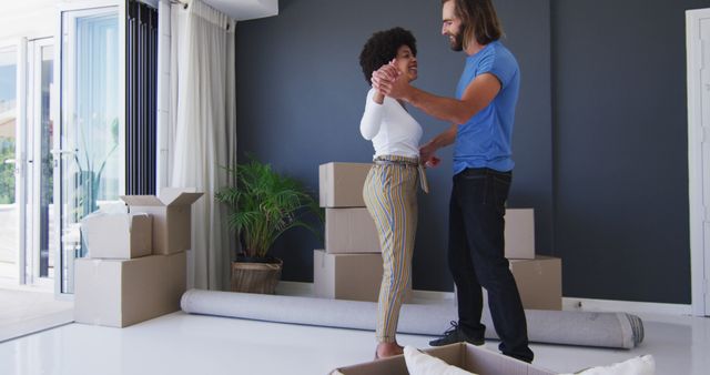 This image shows a joyful couple dancing and enjoying their new apartment surrounded by moving boxes. Use this image for themes related to moving, relationships, new beginnings, and happiness in a new home.