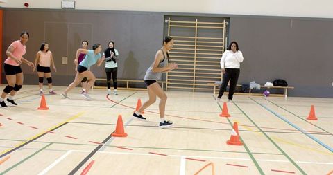 Diverse women sprinting cone drill in indoor gym, dynamic team fitness training