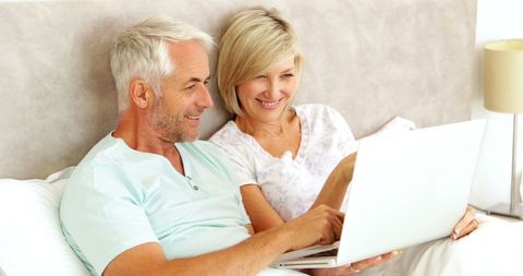 Happy Senior Couple Using Laptop in Bed for Online Browsing