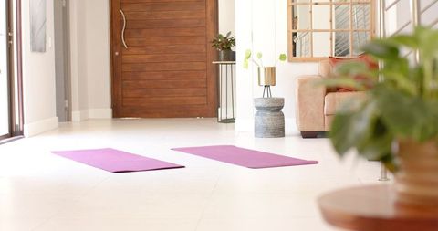 Practicing yoga on purple mats in bright minimal living room with greenery, natural light