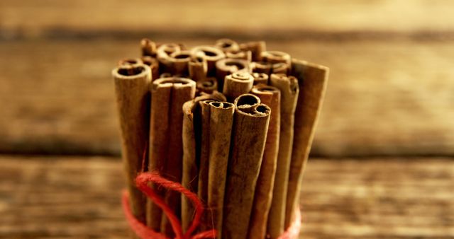 A bundle of cinnamon sticks is tied together with a red string, set against a rustic wooden background. Cinnamon is often used as a fragrant spice in cooking and baking, adding a warm, sweet flavor to dishes.