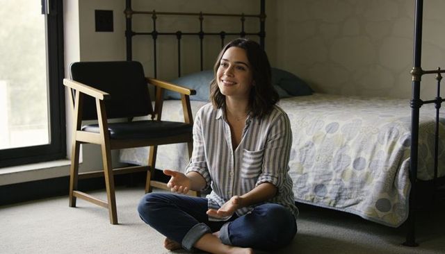 Smiling woman sitting cross-legged on bedroom floor with natural window light