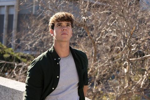 Contemplative young man leaning on urban ledge looking upward among bare trees on campus