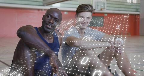 Two male athletes resting on gym court with futuristic holographic data grid overlay
