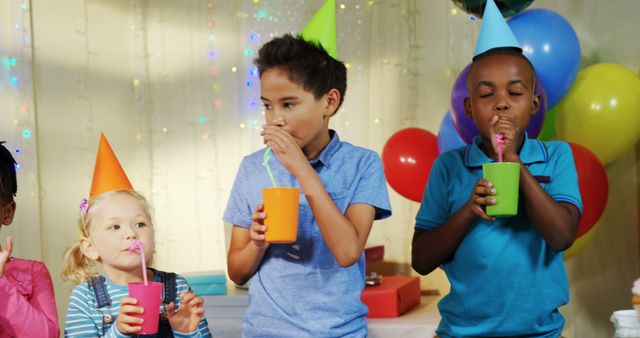 A diverse group of children are enjoying a birthday party, with copy space. They are wearing party hats and sipping drinks, surrounded by colorful balloons and decorations.