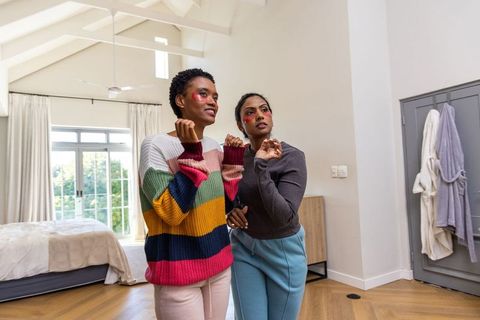 Friends chatting in bright bedroom, indian and african american women sharing skincare moment
