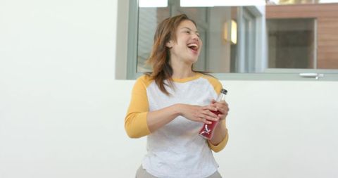 Laughing woman holding red squeeze bottle standing near window casual bright lifestyle