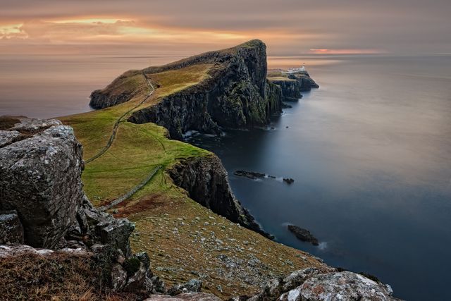 A breathtaking view of a coastal cliff extending into calm sea during a beautiful sunset. Captures natural beauty with a mix of rocky terrain and grassy fields. Perfect for using in travel brochures, nature magazines, or as a decorative print showcasing serene landscapes.