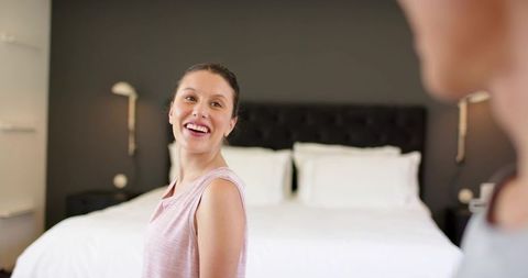 Smiling woman enjoying modern minimalist bedroom with tufted headboard and bright linens