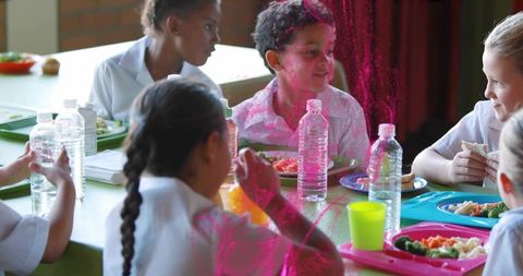 Elementary students sharing lunch and laughing around colorful trays in school cafeteria