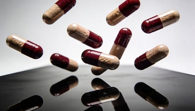 Floating maroon-clear capsules filled with beige granules over glossy black reflection