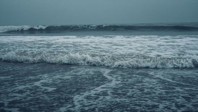 Moody coastal surf crashing and foamy waves lapping dark wet shore under overcast sky