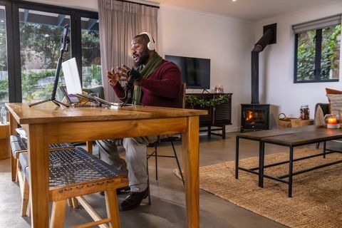 African american man recording cozy home podcast wearing headphones, speaking into microphone