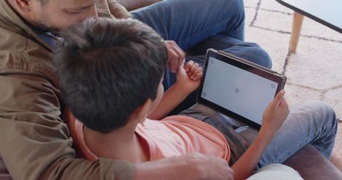 Indian father and son bonding on sofa using tablet for learning and guidance