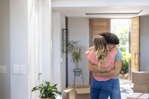 Couple embracing in sunlit entryway during move with unpacked boxes and indoor plants