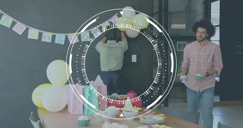 Colleagues decorating modern office breakroom with pastel balloons, cupcakes and gift bags