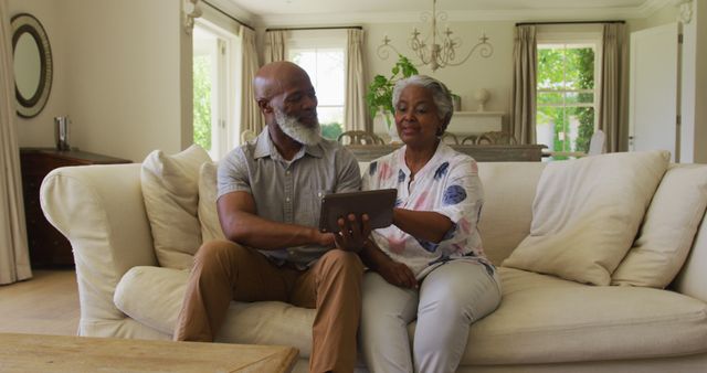 African american senior couple looking at each other and smiling while using digital tablet at home. retirement senior couple lifestyle living concept