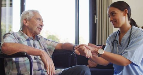Young Nurse Supporting Elderly Man in Wheelchair at Home