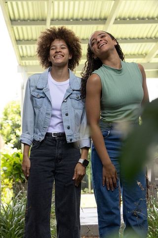 Smiling african women friends standing under sunlit porch roof wearing denim