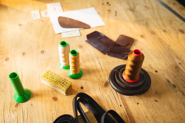 High angle view of thread spools, leather and brush on wooden workbench in workshop. unaltered, small business, equipment, still life, handcraft, leather craft and workshop.