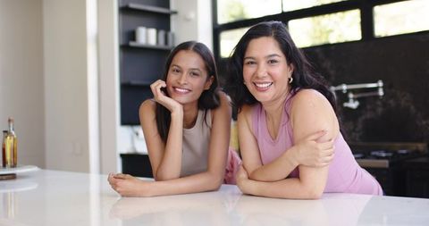 Smiling diverse women leaning on contemporary kitchen island, casual daylight lifestyle