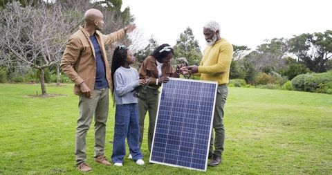 Multigenerational family inspecting solar panel and cables in park for sustainability lessons