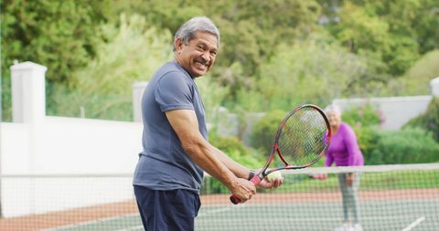 Happy Senior Man Playing Tennis Outdoors on Sunny Day
