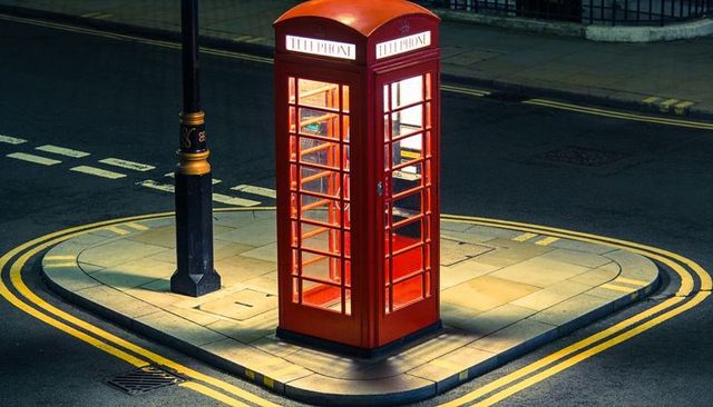 Red british telephone booth casting warm light on traffic island with double yellow lines