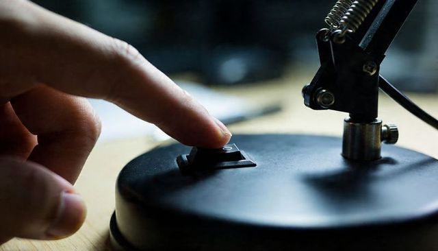 Finger pressing lamp switch closeup on matte black base macro detail for lighting control
