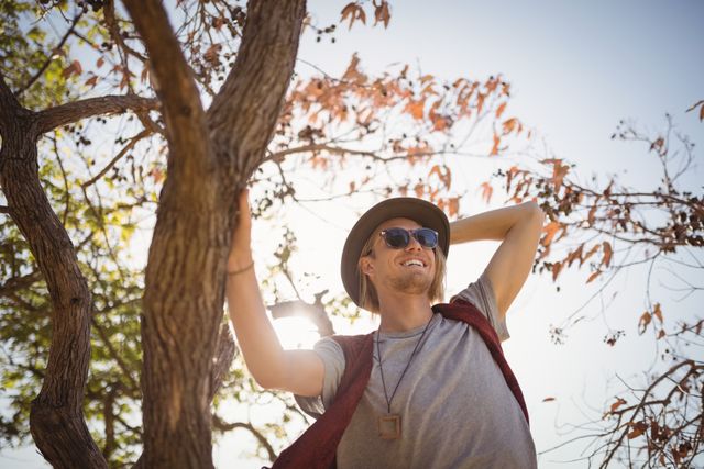 Low angle view of smiling man standing on tree against sky during sunny day