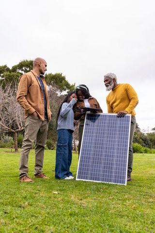 Multigenerational african american family examining solar panel in backyard with tablet