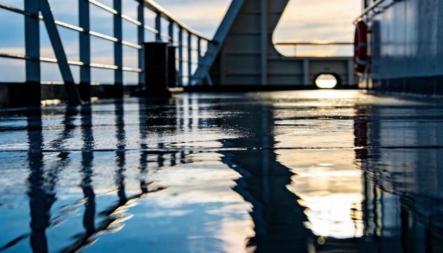 Sunlit wet ship deck reflecting railings and horizon, low angle nautical perspective