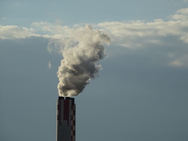 Industrial smokestack emitting smoke against cloudy sky conveys themes of pollution, environmental impact, and climate change. This is suitable for use in articles, reports or educational materials about industrial emissions, environmental policies, and sustainability efforts.