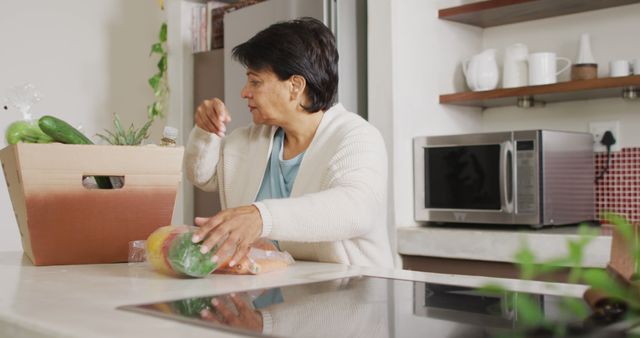 Senior biracial woman grabbing vegetables from box in kitchen alone. healthy and active retirement at home.