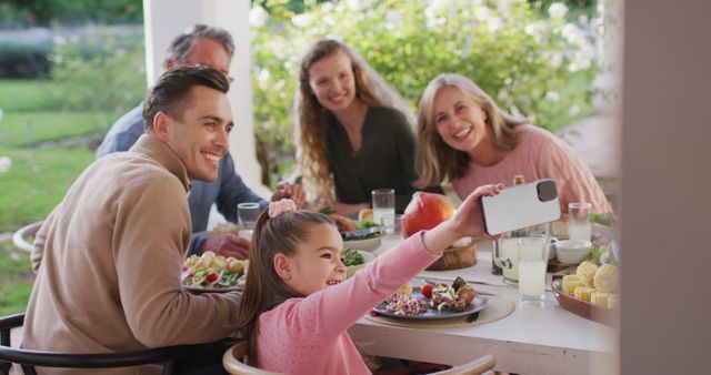 Image of happy caucasian parents, daughter and grandparents taking selfie at outdoor dinner table. Family, domestic life and togetherness concept digitally generated image.