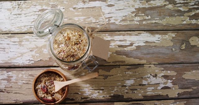 A jar of granola is placed next to a bowl filled with the same, ready for a healthy meal, with copy space. Rustic wooden background adds a natural and vintage feel to the presentation of the wholesome snack.