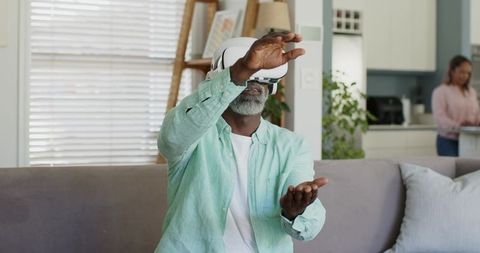 Senior man exploring virtual reality at home using vr headset on cozy living room sofa