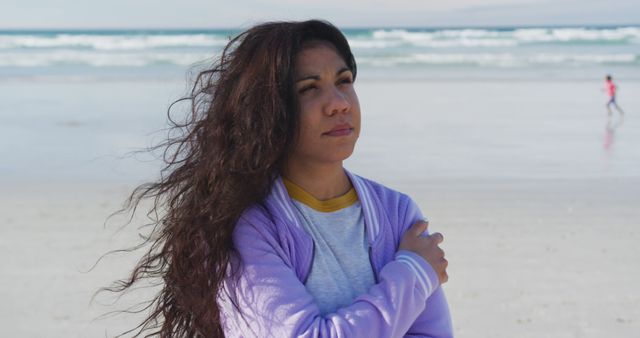 Woman with windblown hair standing on beach with ocean in background. She appears to be in deep thought, embodying a reflective mood. Can be used for themes of contemplation, nature, solitude, and introspection.