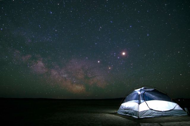 This depicts a tent set up under a dark, starry night sky with the Milky Way clearly visible. The setting suggests a remote location, perfect for stargazing, astronomy enthusiasts, and lovers of nature and outdoor adventures. Ideal for use in promotional materials for camping gear, travel and adventure blogs, or inspirational posters highlighting the beauty of the wilderness.