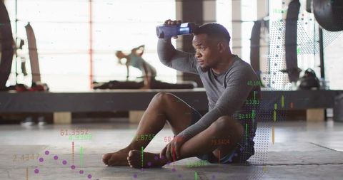 Tired athlete cooling forehead with water bottle while resting in gym with fitness data overlay