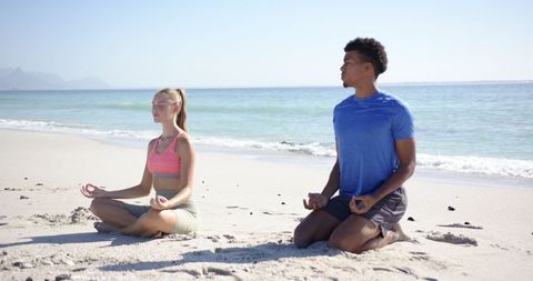 Couple Meditating on Sandy Beach under Blue Sky