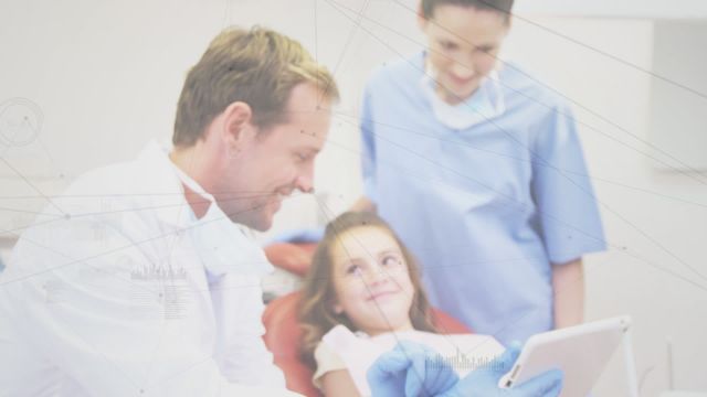 Image showing a dentist engaging with a young girl using a tablet, possibly explaining procedures or showing her images. Ideal for illustrating child-friendly dental practices, technological advancements in health care, or highlighting family-centric medical environments.