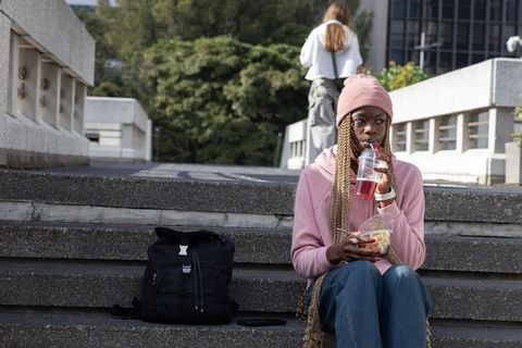 African-american woman sitting on campus steps sipping red drink and eating salad