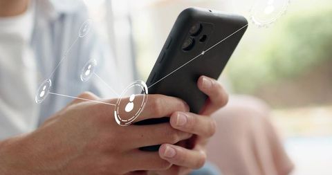 Young man holding smartphone tapping screen with social network overlay in lounge